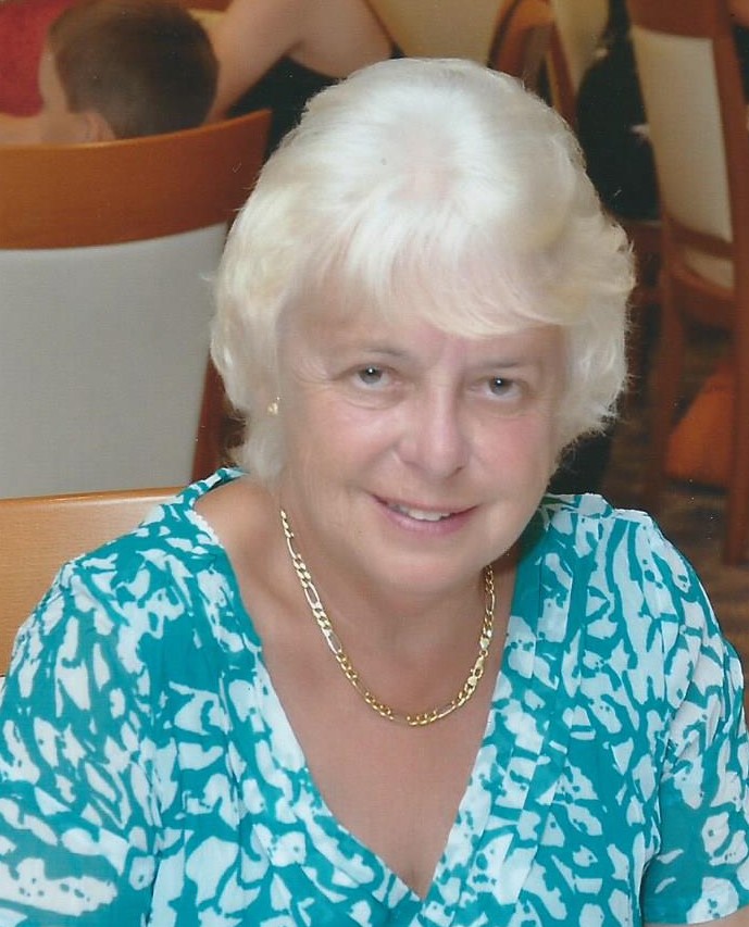 Woman with white hair wearing a turquoise and white top smiling at the camera